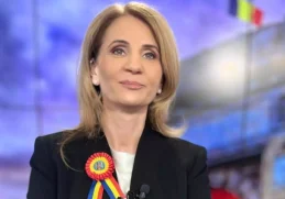 Jurnalista Anca Alexandrescu, purtând o bluză neagră și o insignă tricoloră, în timpul unei emisiuni.