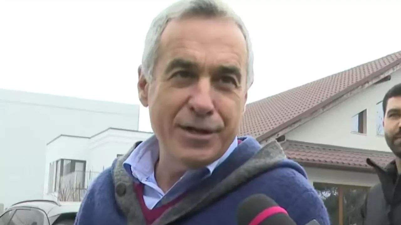 Călin Georgescu vorbind cu reporterii în exterior, purtând un gilet gri și o cămașă albastră, cu o expresie preocupată pe față