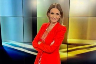 Anca Alexandrescu în studio, purtând un costum roșu, zâmbind în timp ce se pregătește pentru o emisiune la Realitatea PLUS, dezvăluind manipulările din politica românească.