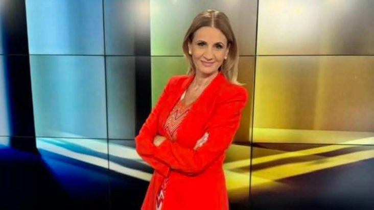 Anca Alexandrescu în studio, purtând un costum roșu, zâmbind în timp ce se pregătește pentru o emisiune la Realitatea PLUS, dezvăluind manipulările din politica românească.