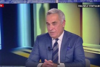 Călin Georgescu participă la emisiunea 'Culisele Statului Paralel' la Realitatea Plus, îmbrăcat în costum albastru și cravată, discutând serios despre relațiile internaționale și viitorul NATO
