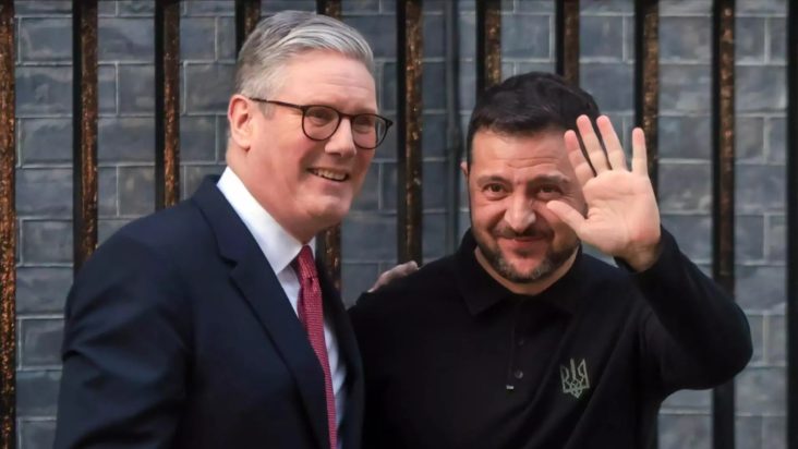 Premierul britanic Keir Starmer alături de președintele ucrainean Volodimir Zelenski, zâmbind și salutând, în timpul unei întâlniri la Londra
