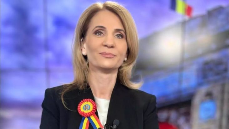 Anca Alexandrescu, prezentatoarea emisiunii Culisele Statului Paralel, zâmbind în timp ce poartă o cocardă tricoloră, reprezentând demnitatea și patriotismul în mass-media românească.
