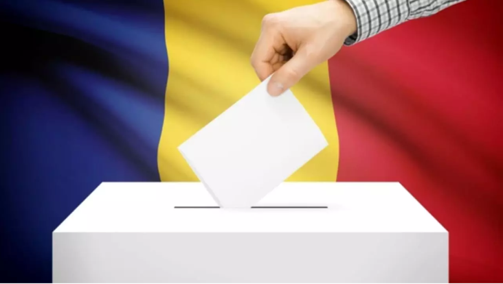 O persoană introduce un buletin de vot într-o urnă albă, având în fundal tricolorul României, simbolizând participarea la un proces electoral democratic