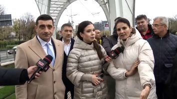 Anca Alexandrescu și George Simion la stația de tramvai Eroii Revoluției, criticând investiția de 5,3 milioane de euro într-o structură decorativă, în timp ce bucureștenii așteaptă tramvaiul în frig și ploaie.