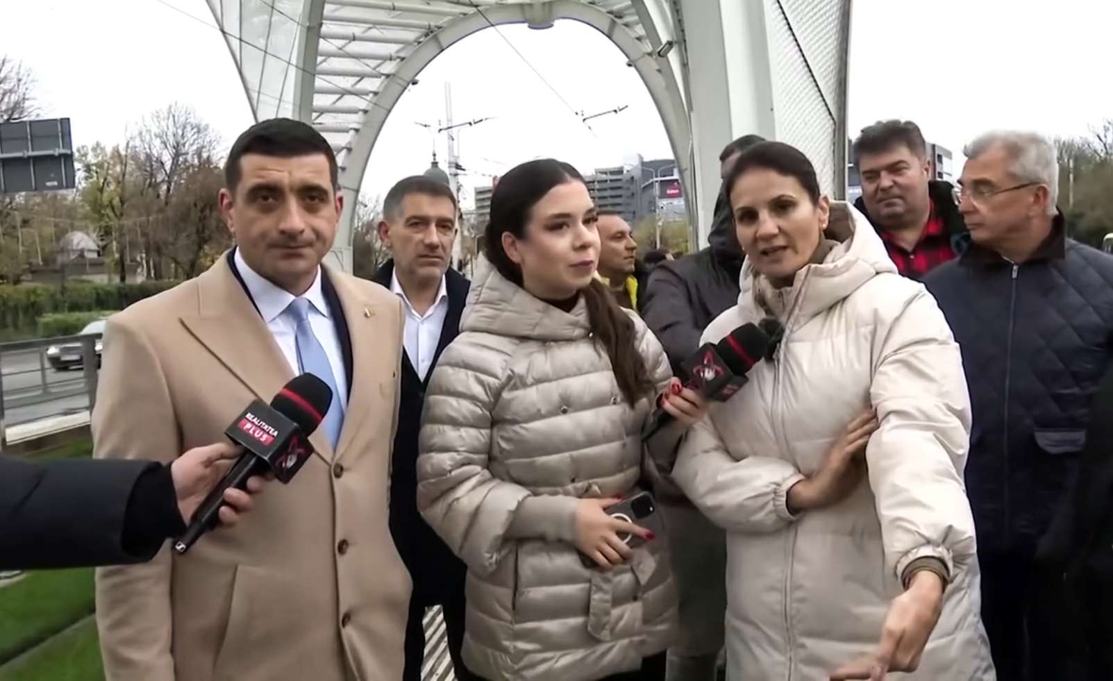 Anca Alexandrescu și George Simion la stația de tramvai Eroii Revoluției, criticând investiția de 5,3 milioane de euro într-o structură decorativă, în timp ce bucureștenii așteaptă tramvaiul în frig și ploaie.